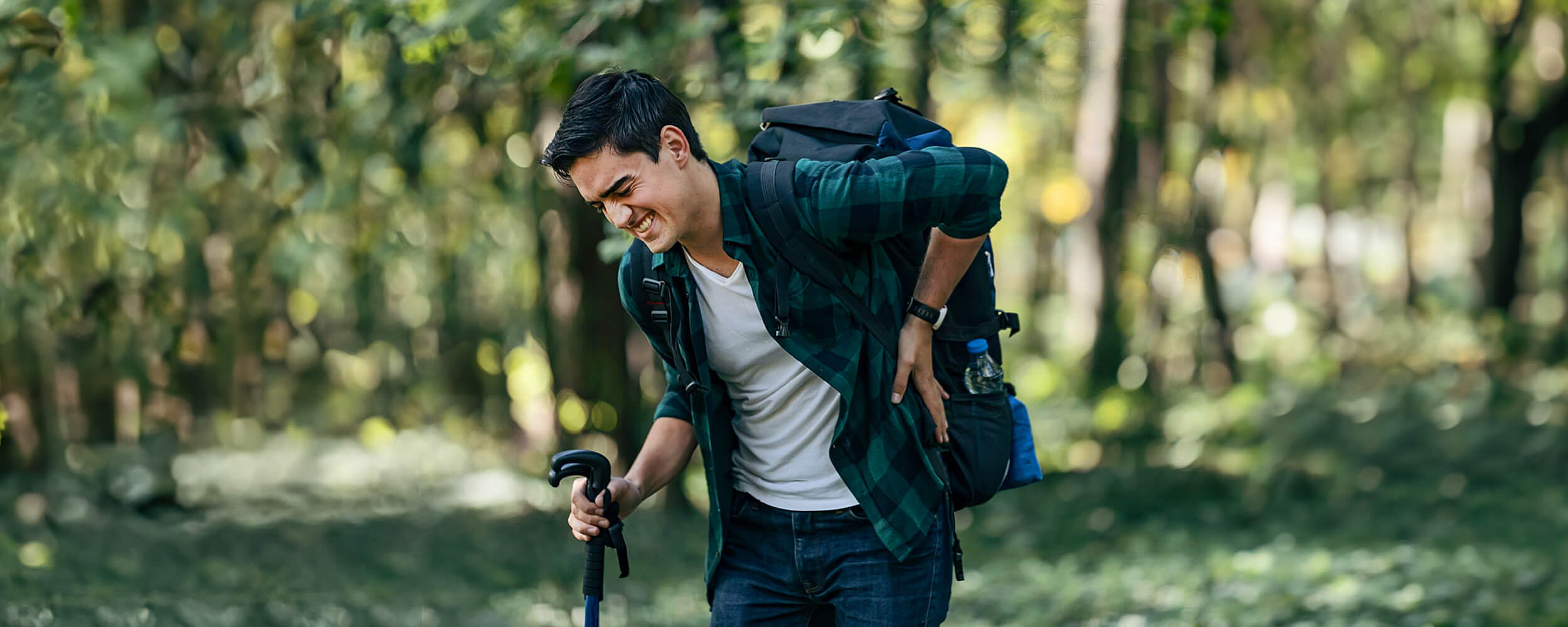 Asian man holding back in pain and in hiking gear