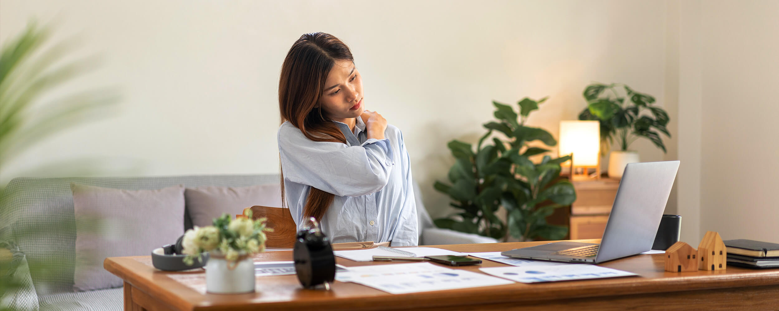 Woman holding shoulders sitting behind a desk with work